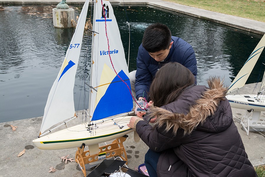 Two students prepare sailboat to race in fountain