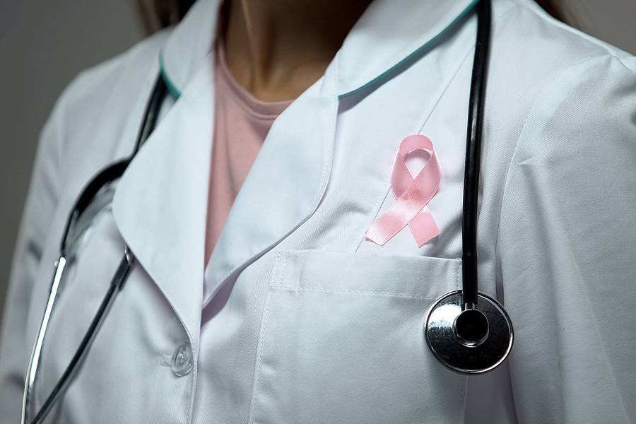 Female doctor wearing pink breast cancer ribbon on her white medical coat
