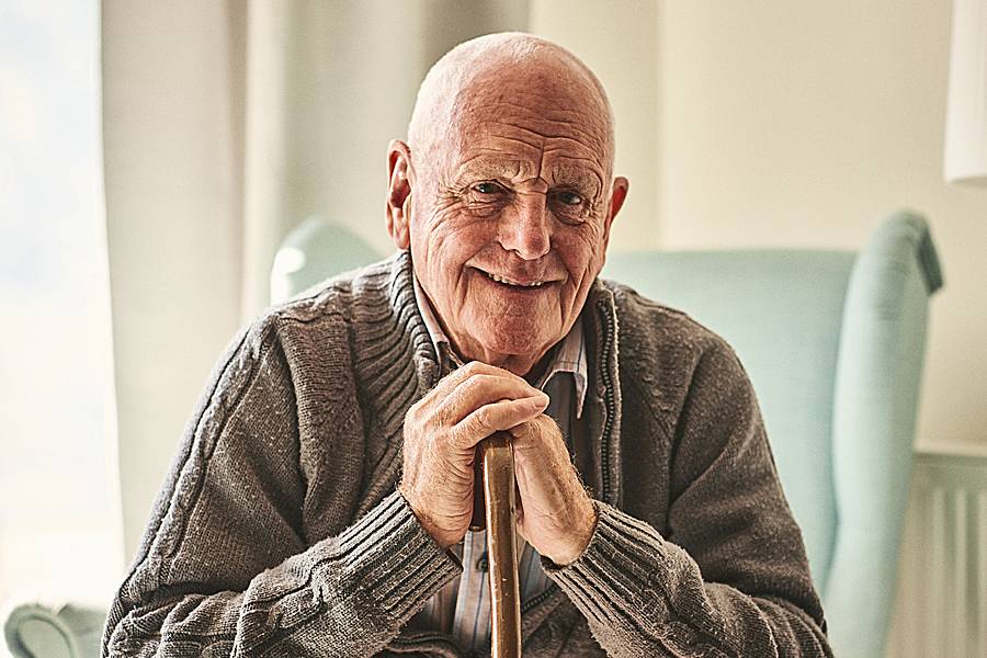 Smiling elderly man sitting at home leaning on cane