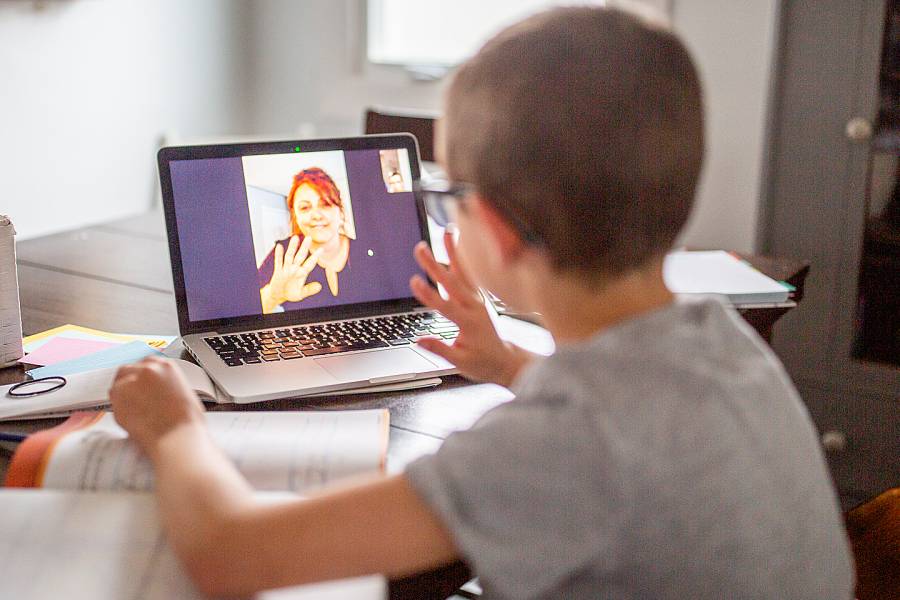 Young boy waving to a teacher on his laptop screen
