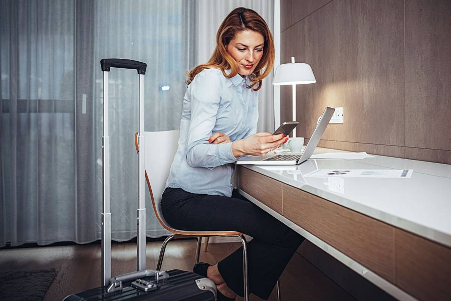 Woman in hotel room working with her laptop and mobile phone
