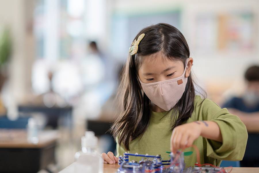 Young girl wearing a medical mask and playing with toys in a day care setting