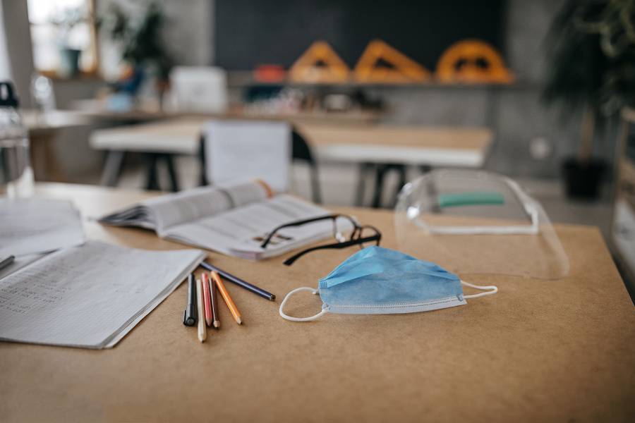 A classroom desk with school supplies and a mask