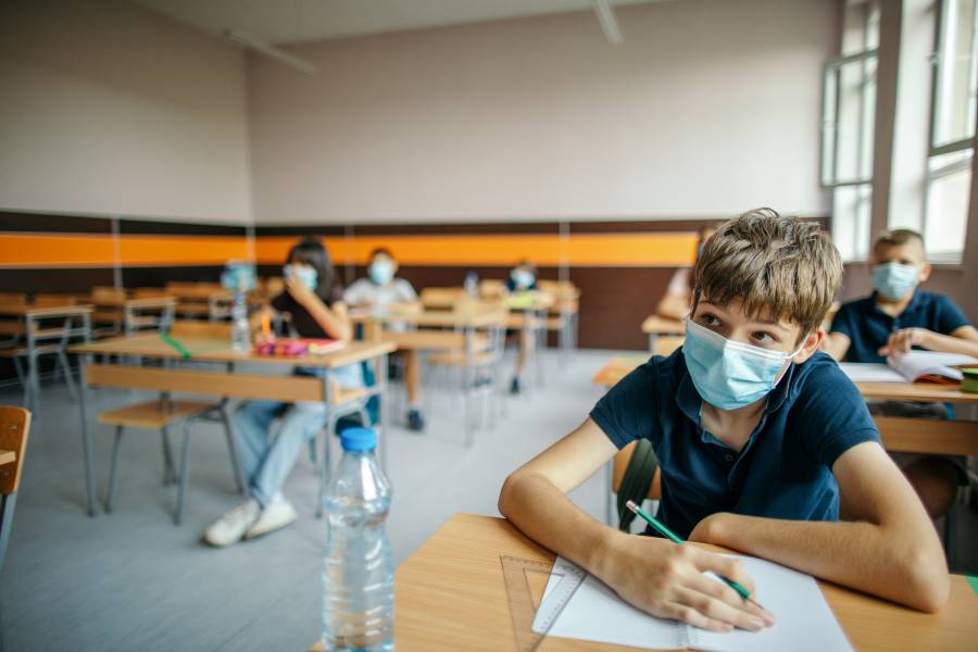 Students with protective masks sitting in school desks in their classroom. 