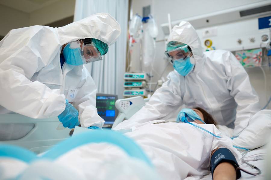 Health care workers in personal protective equipment assist a patient