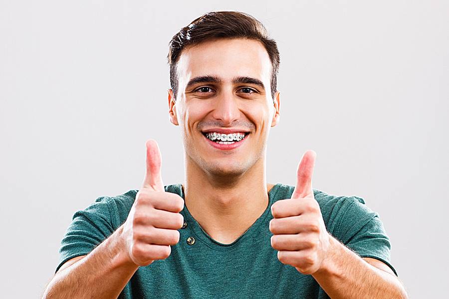 Smiling man wearing braces on his teeth gives two thumbs up