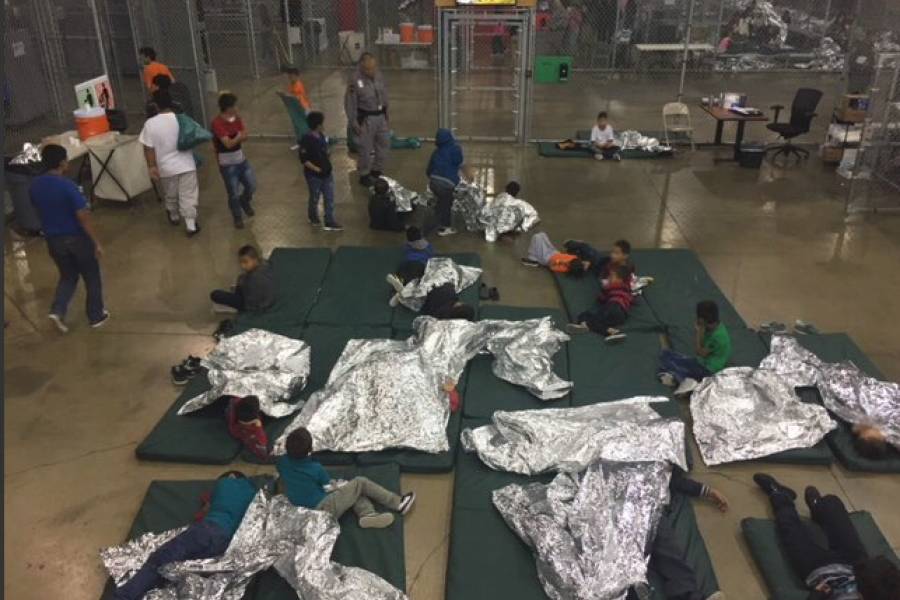 Children sit on mats with shiny silver blankets at a detention facility