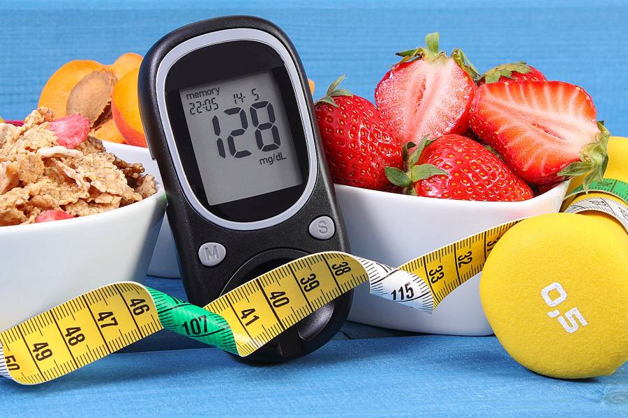 Glucose monitor, measuring tape, and a bowl of strawberries