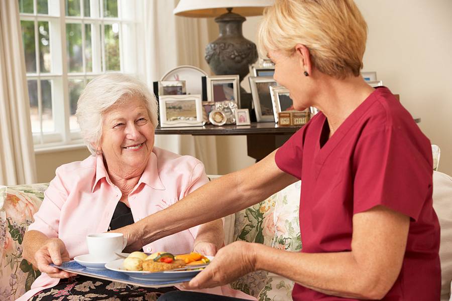 Helper serving senior woman with meal in care home