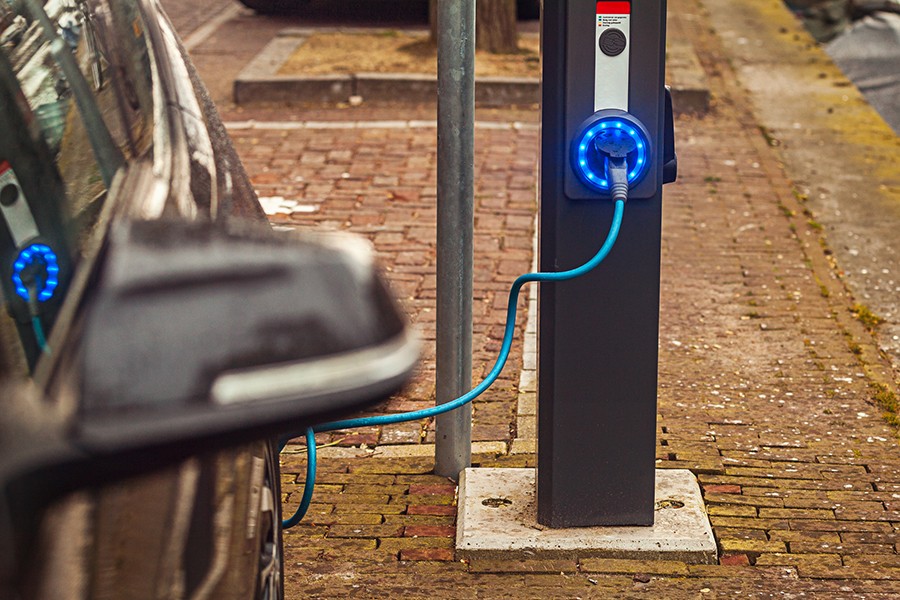An electric car is plugged into a charging station which is lit with blue LED lights