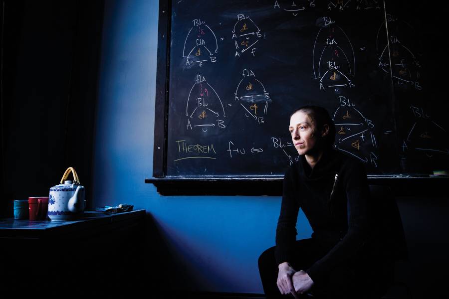 Emily Riehl sits in front of a chalkboard covered in mathematic equations