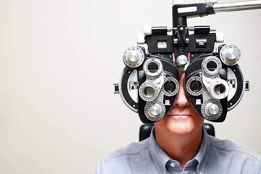 Man looking through an ophthalmic instrument called a phoroptor