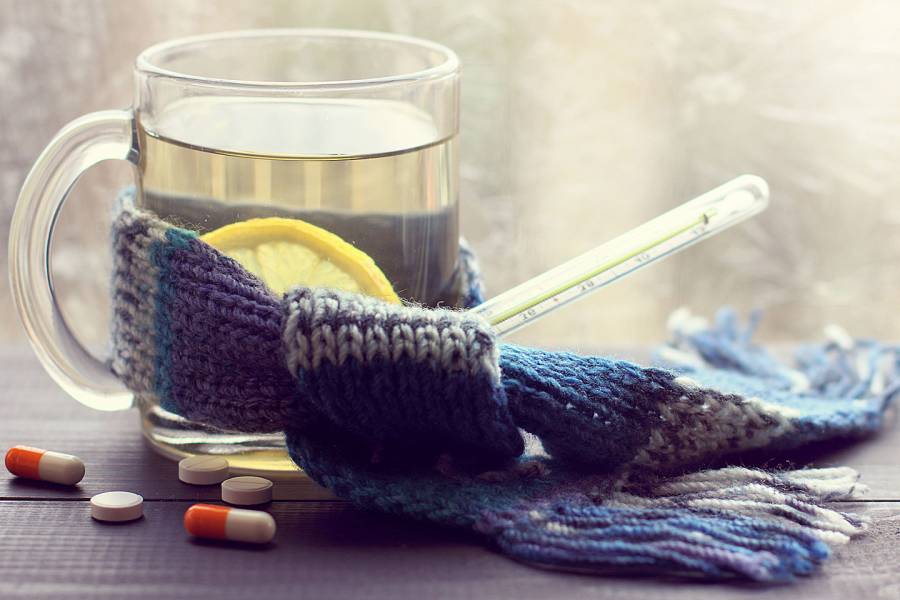 Mug of hot water with lemon and a thermometer wrapped in a knitted scarf