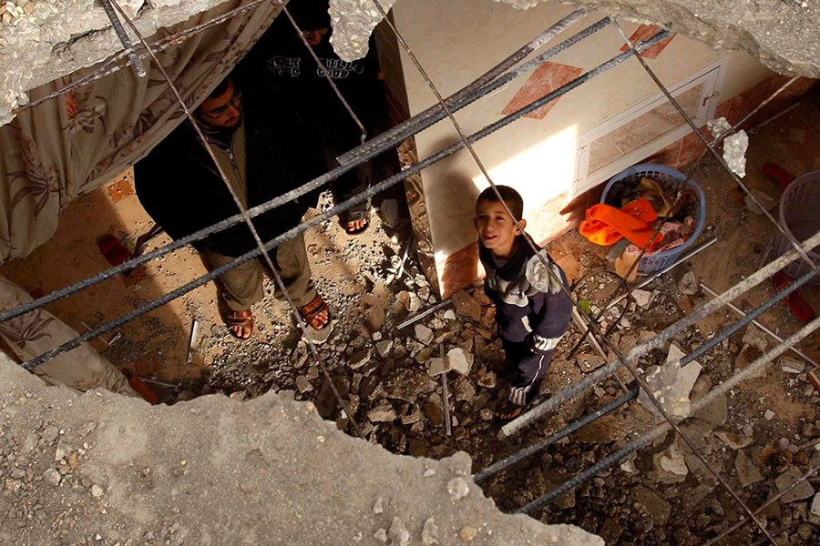 A little boy looks up through the bombed ceiling of his home