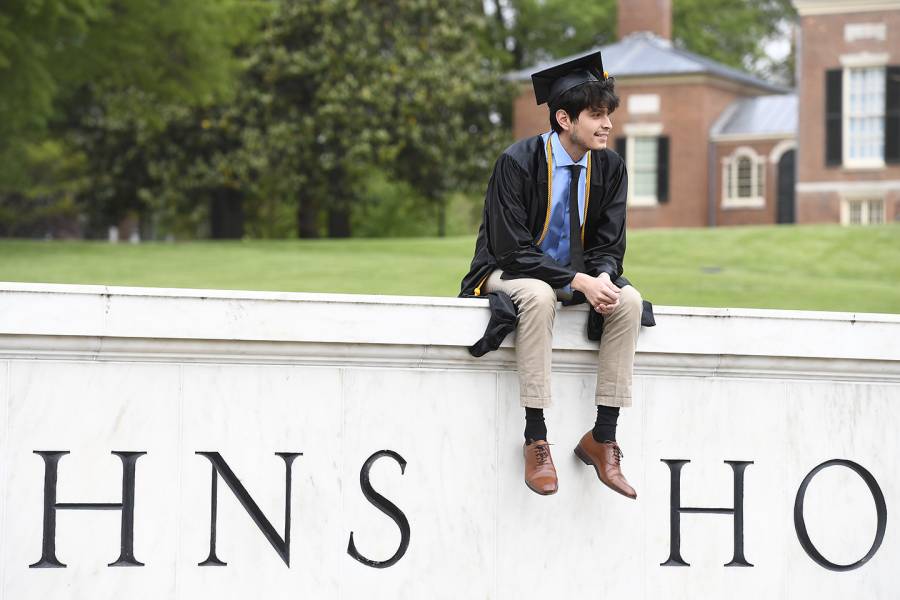 Graduate sits on the Johns Hopkins gateway sign