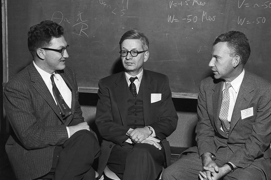 Black and white photo: Three men chat in front of a blackboard with mathematical equations
