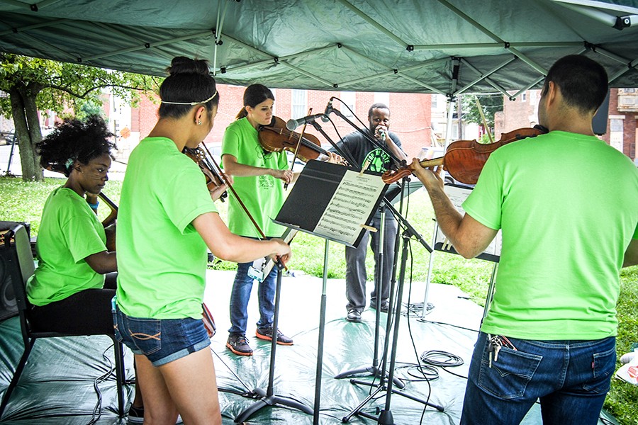 String quartet players in lime green t-shirts perform under a tent