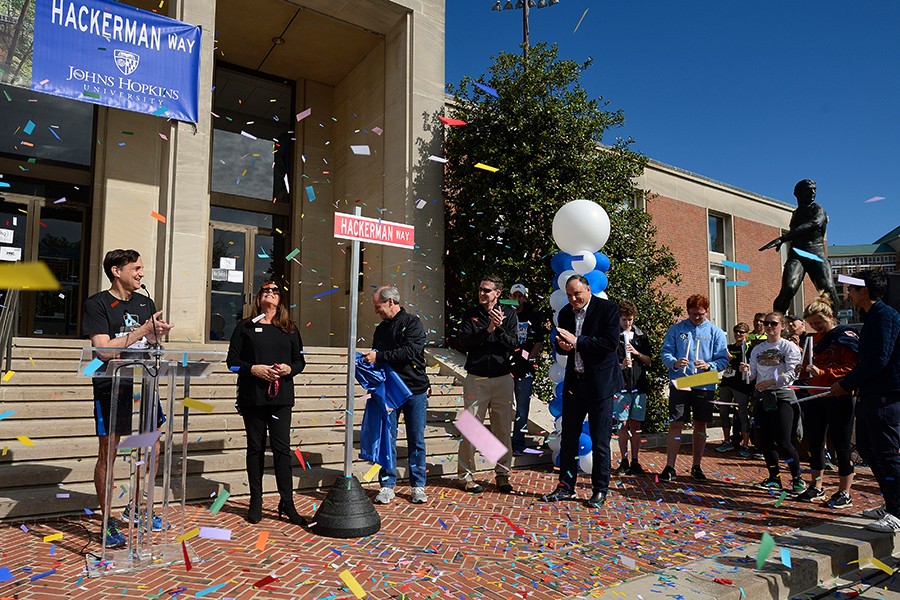 Several people stand on a brick sidewalk as multicolored confetti falls all around them