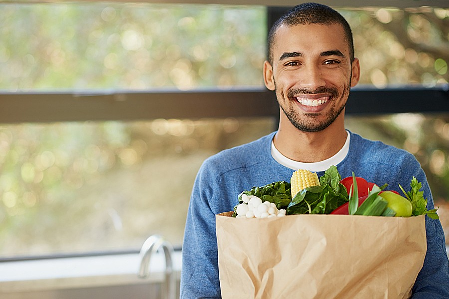 Photo of smiling man carrying a grocery bag of fresh vegetables.