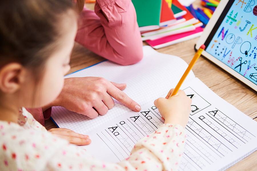 Child care professional helping a 5-year-old girl write the alphabet