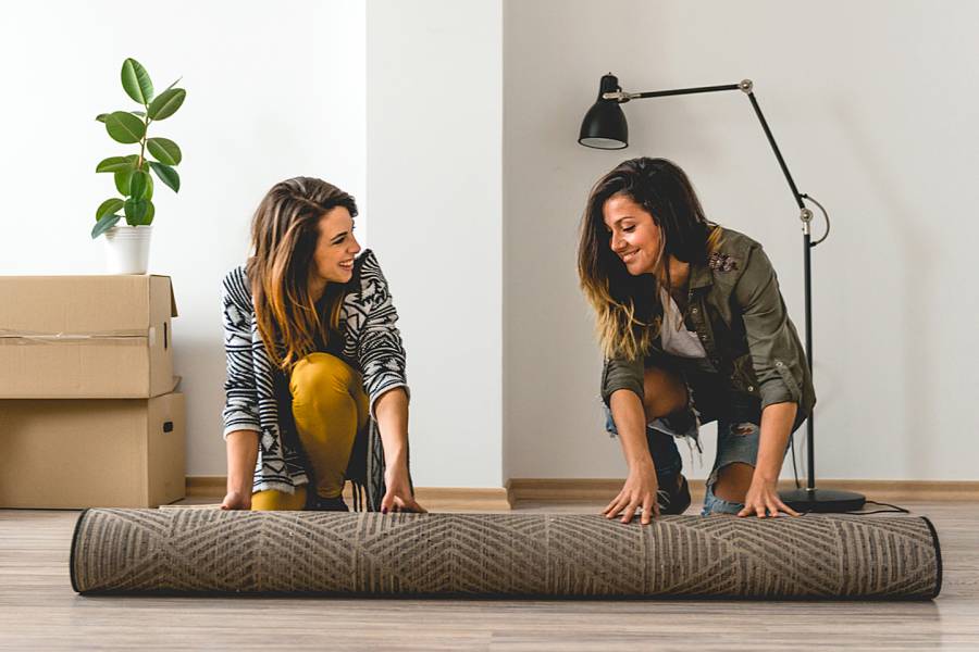 Two women unrolling a rug in their new apartment