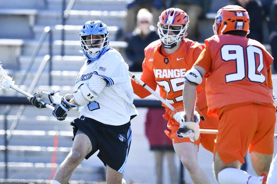 Hopkins lacrosse player winds up for a shot against two Syracuse defenders