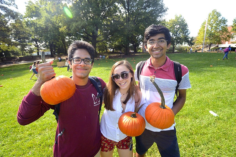 Three students pose for a photo while holding pumpkins
