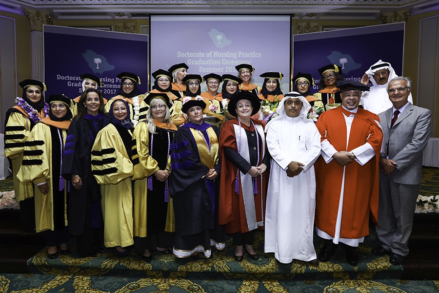 A group of people all wear graduation regalia, some of whom also wear traditional Saudi garbs