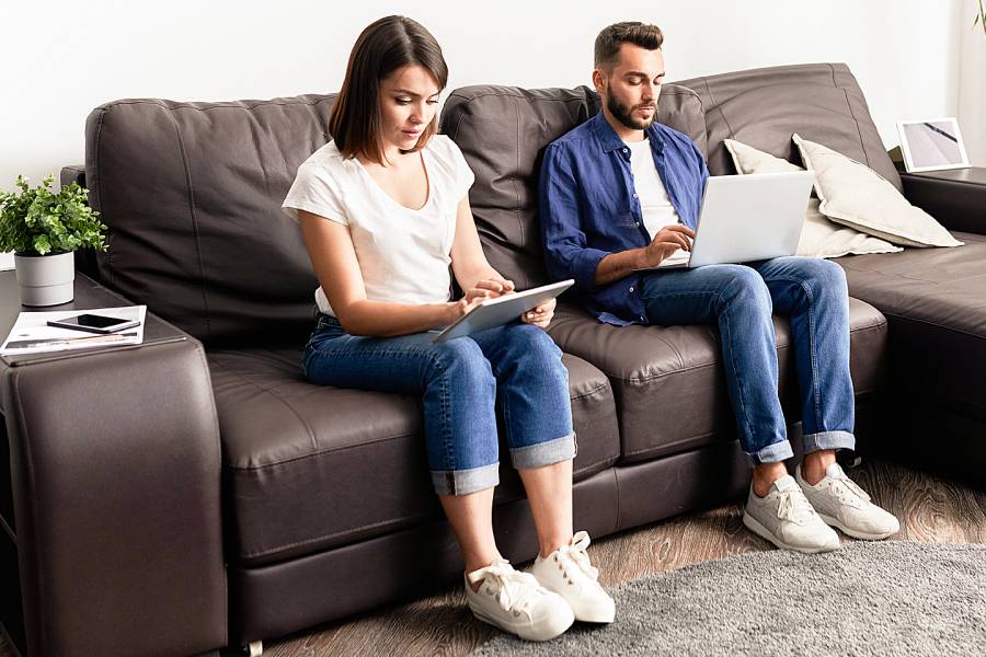 Woman and man next to each other on couch with laptops