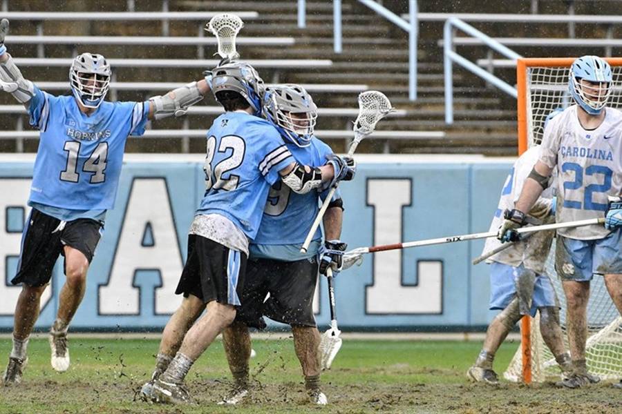 Johns Hopkins players celebrate a goal on a muddy field at North Carolina