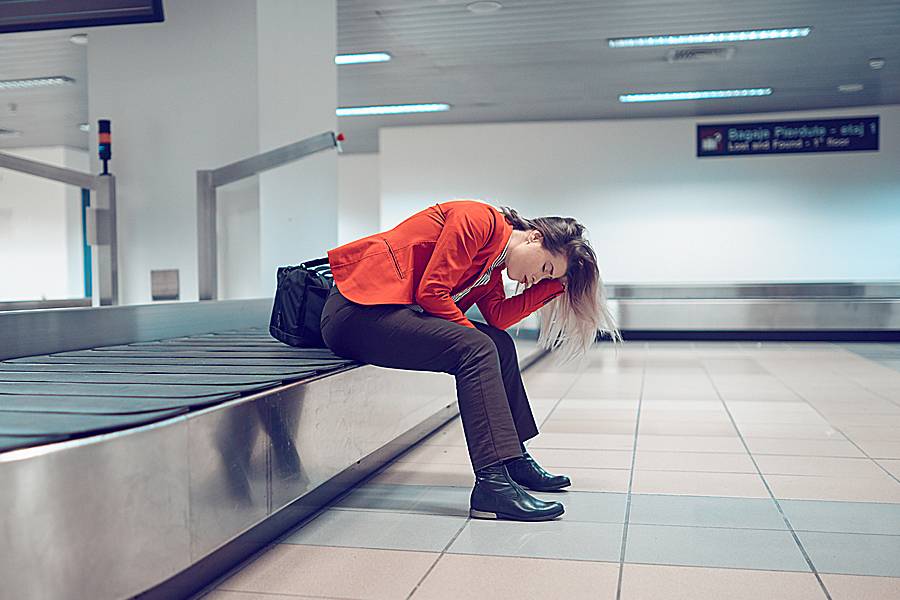 Frustrated woman sitting in the airport on an empty conveyer belt, having lost her luggage