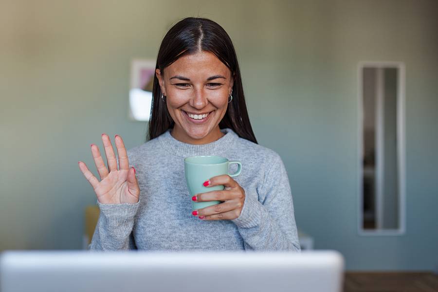 Young woman at home waving to her computer screen