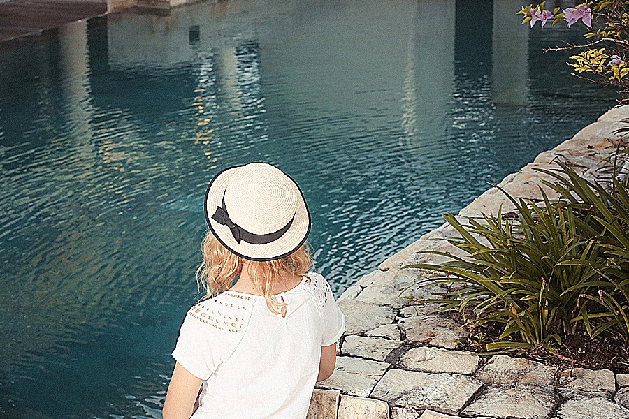 Photograph of a woman in a straw hat contemplating a peaceful-looking body of water