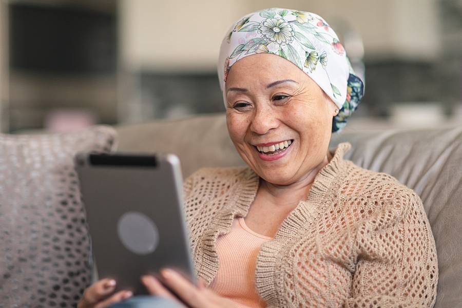 Woman with head wrapped in scarf smiling at the tablet she’s watching
