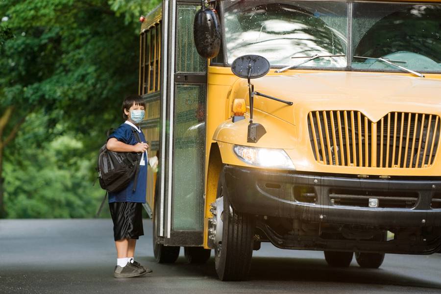 A masked boy boards a school bus