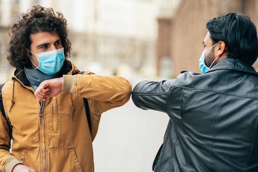 Two men in medical masks bump elbows in greeting