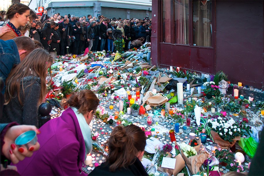 Crowd around memorial of candles, flowers on Paris sidewalk