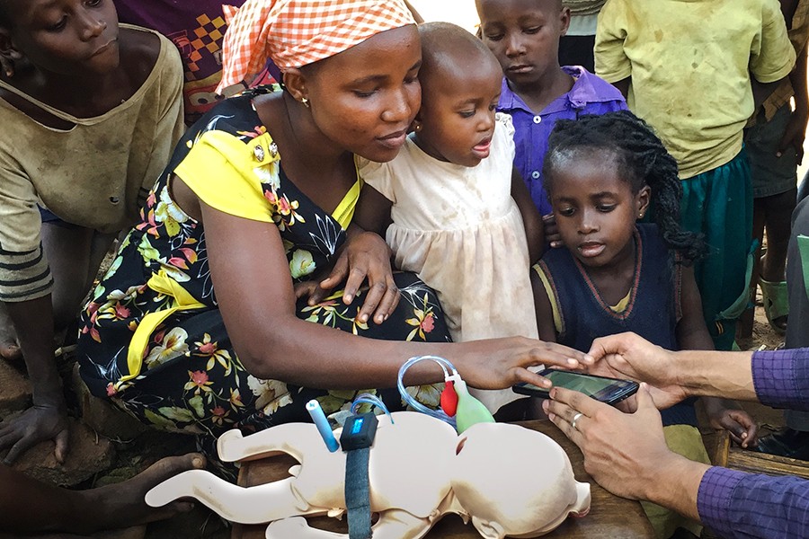 A mother in Uganda examines a cell-phone-like device next to an infant manikin