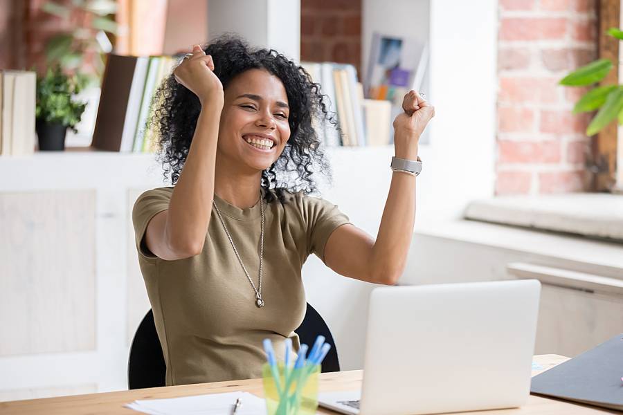 Happy employee looking at laptop and celebrating with arms raised