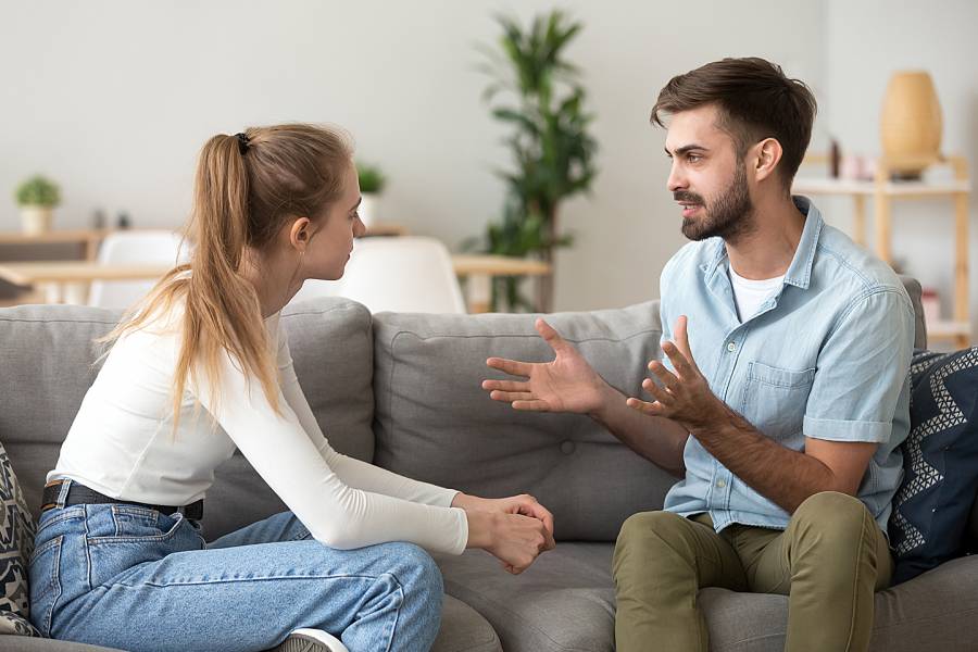 Young man and woman sitting on couch having a serious conversation