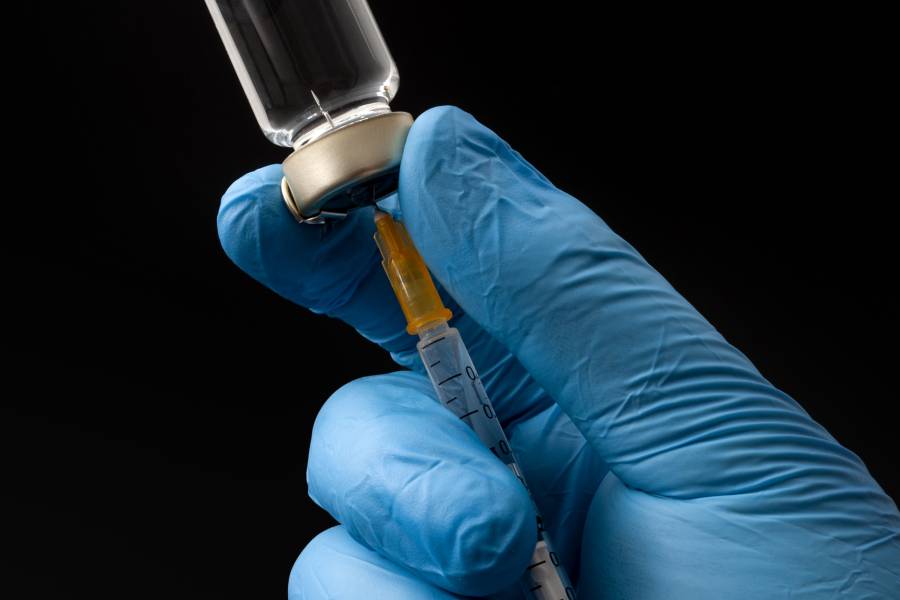A photo of a gloved hand filling a syringe from a vial of clear liquid