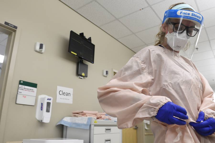 A nurse dons a surgical gown and wears a face mask as well as a face shield