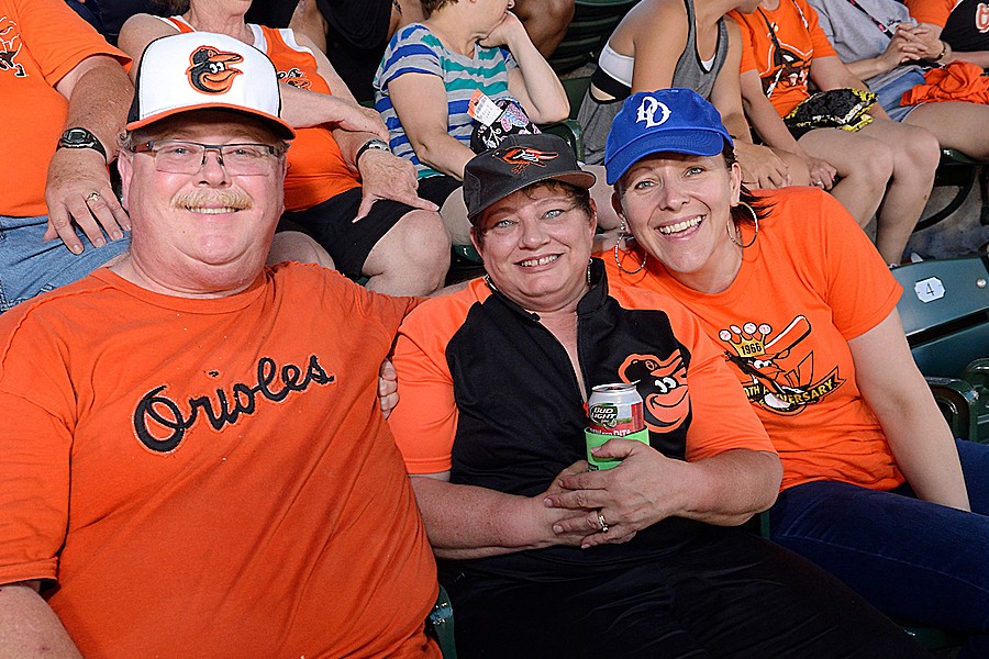 Three people in Orioles T-shirts photographed at a game