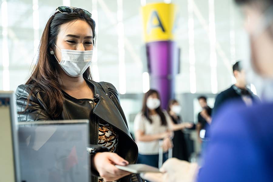 Woman wearing a protective medical mask hands documents to an airline ticket agent.