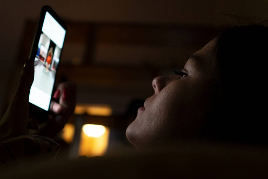 A woman scrolls on her phone while in bed