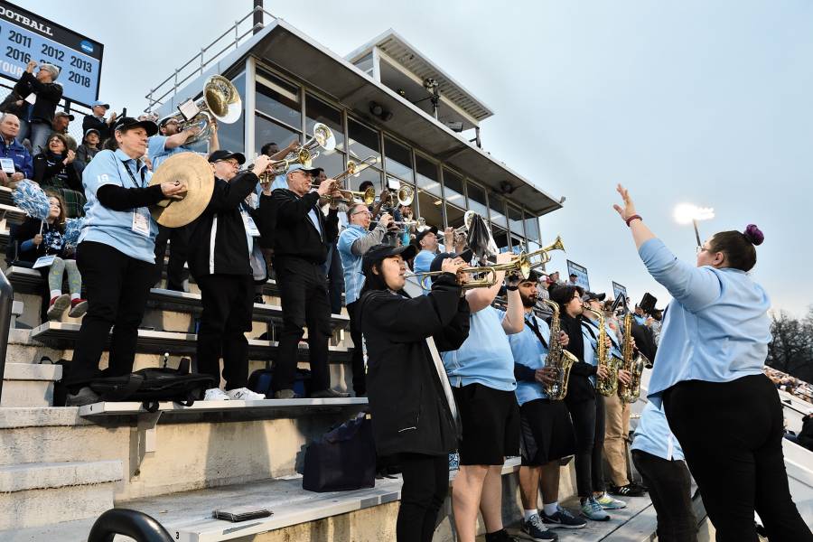 Emily Joseph conducts the JHU pep band, which consists of trumpet players, saxophonists, and others in the stands at Homewood Field