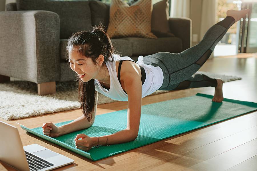Woman on yoga mat doing a plank exercise while watching a laptop