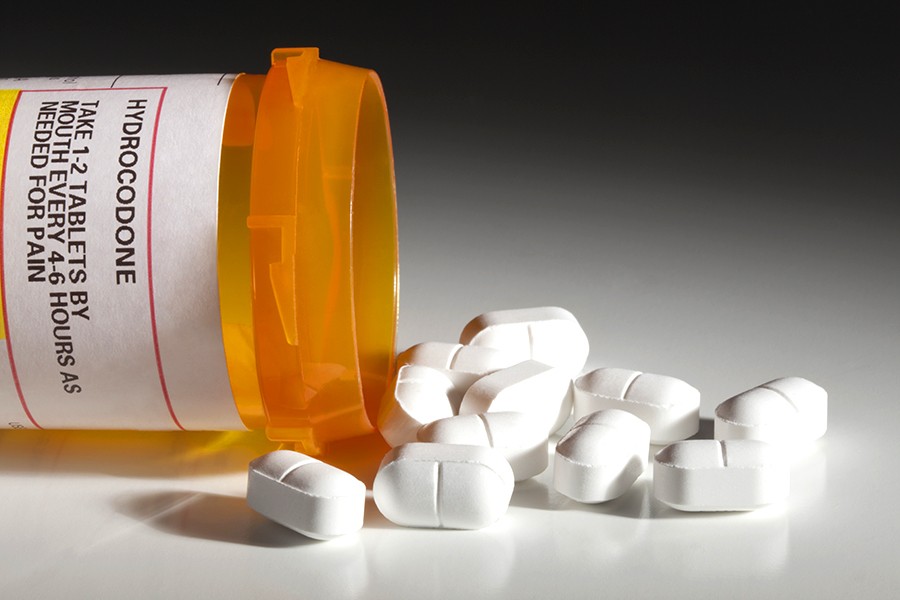 Orange prescription bottle labeled 'hydrocodone' with white pills spilling out 