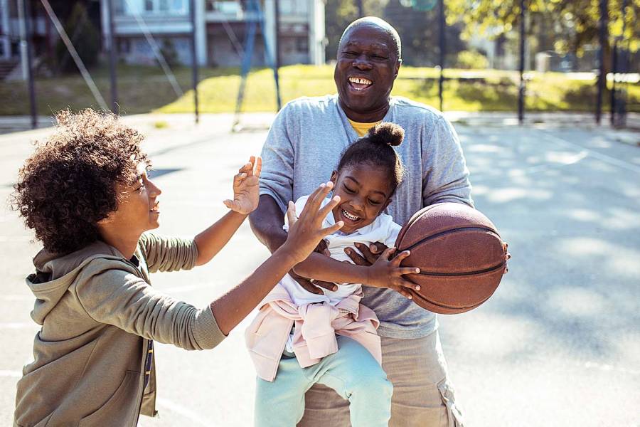A grandfather playing basketball with his young grandson and granddaughter.