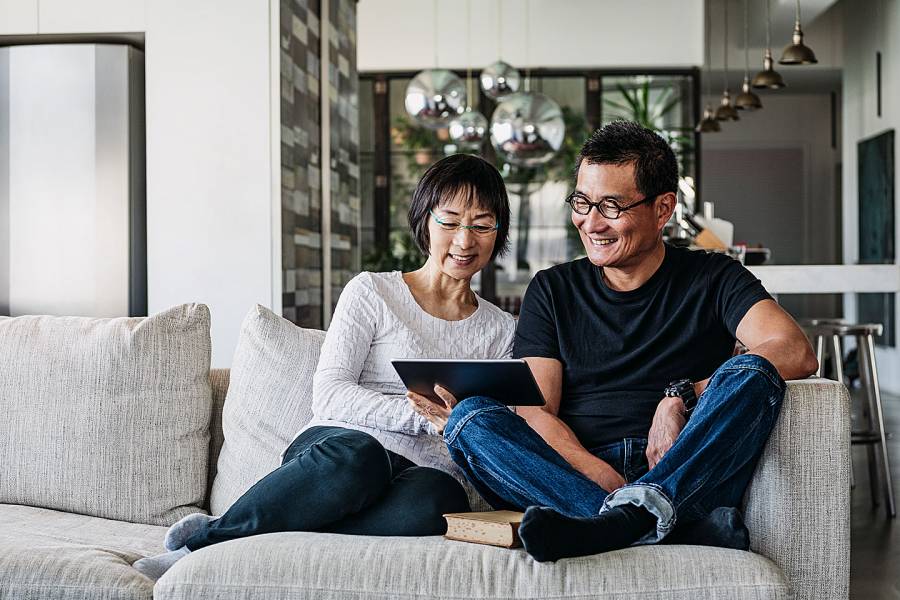 Smiling older couple sitting on a couch looking at a tablet 